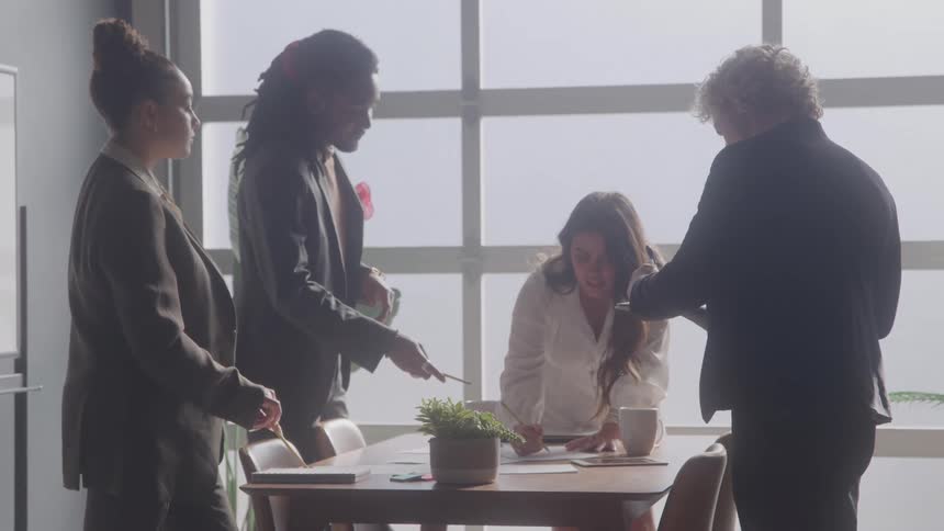 Four people interact around a table during a meeting lit by natural light