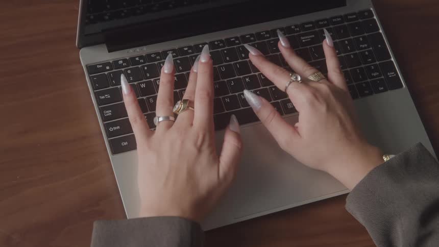 Hands with long nails and rings typing on a laptop keyboard