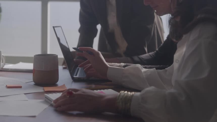 People gathered at a table using a laptop and making notes in a notebook