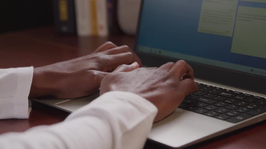The video shows a closeup of a persons hands typing on a laptop keyboard the screen of the laptop is visible in the background with a postit note application open