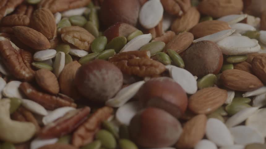 The video shows a closeup of a variety of nuts and seeds including almonds pecans hazelnuts and pumpkin seeds the pile of nuts and seeds is shown in clear detail and is slowly rotating