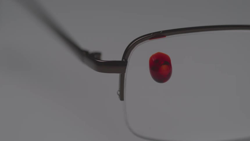 A red droplet across the lens of a pair of eyeglasses set against a blurry lightcolored background