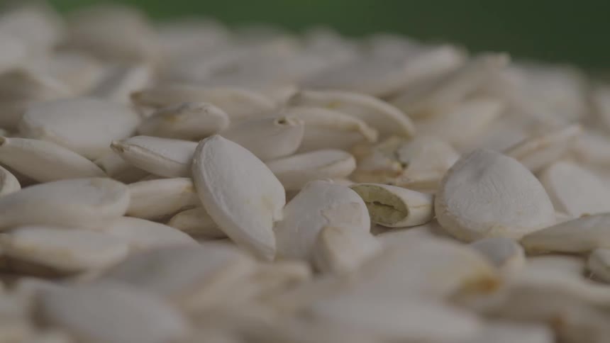 Pumpkin seeds in their shells fall to cover a surface