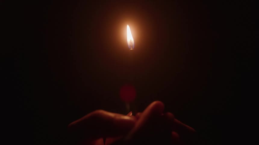 A persons hand holding a lit candle in a dark room