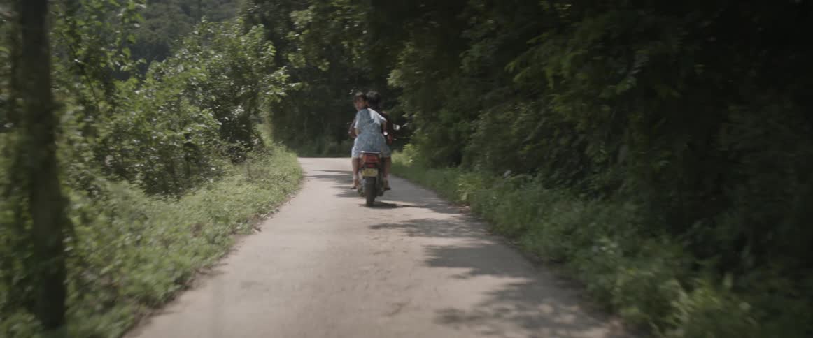 People ride down a small trail on a scooter