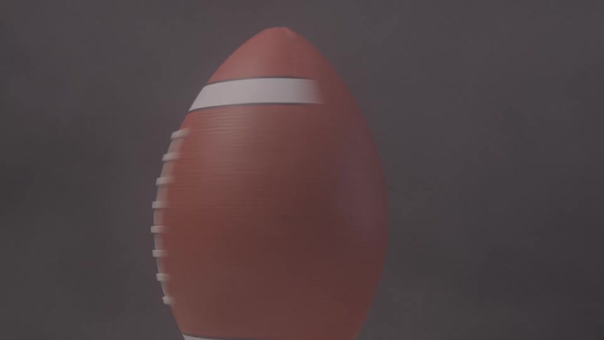 A close view of an american football spinning vertically in the air with the white laces and stripes blurred by the motion