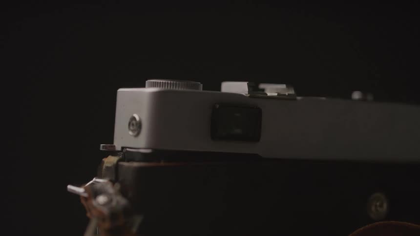 A partially blurred closeup shows the top of a vintage camera against a dark background