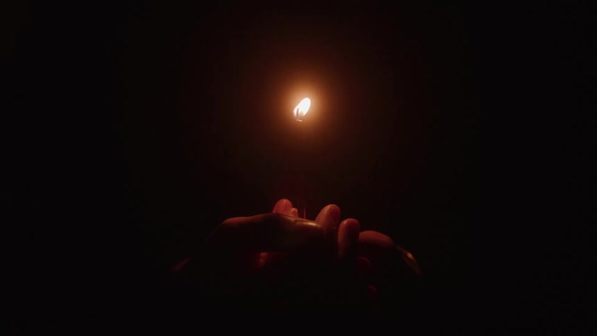 A single match flame held by hands in the darkness flickers and then is extinguished