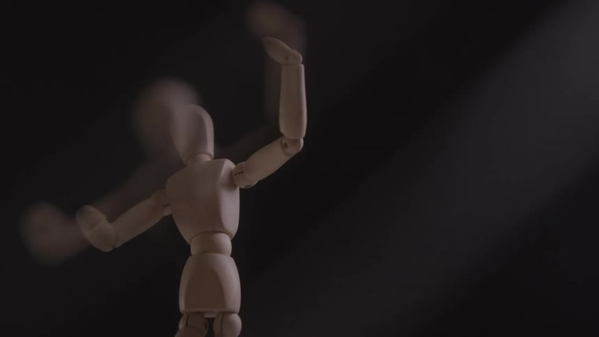 The video shows a wooden mannequin or artists model standing upright against a dark background its a closeup shot that focuses on the figures torso and head which are slowly bobbing back and forth