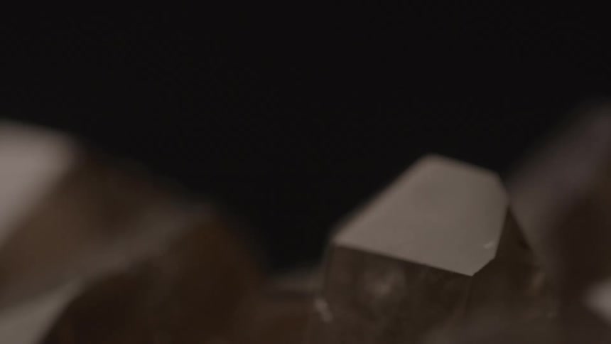 The video shows a closeup of a few smoky quartz crystals which are a translucent brown color the crystals are rotating slowly against a dark background and light is reflecting off their facets