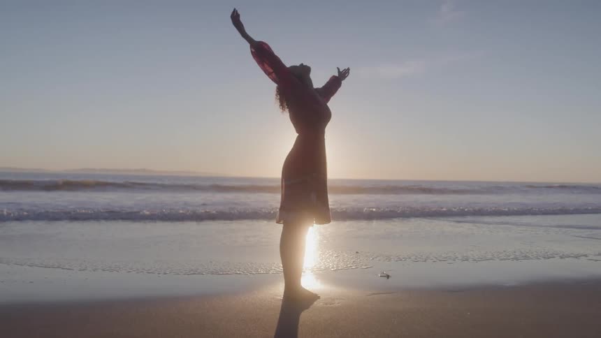 Woman in dress spreading her arms while standing on the beach in the morning