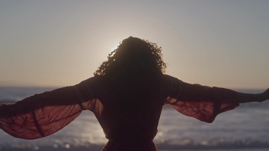 Woman in a dress opening her arms while standing on the beach in the late afternoon