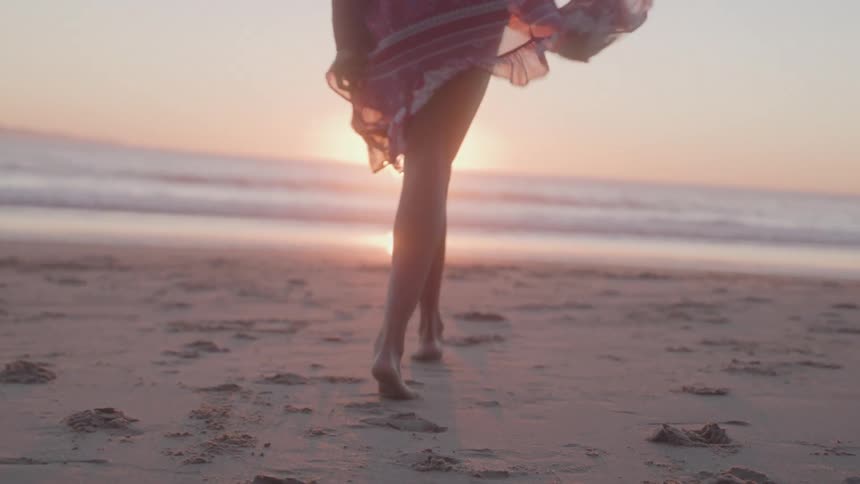 Person walks barefoot on the sand towards the sea during sunset