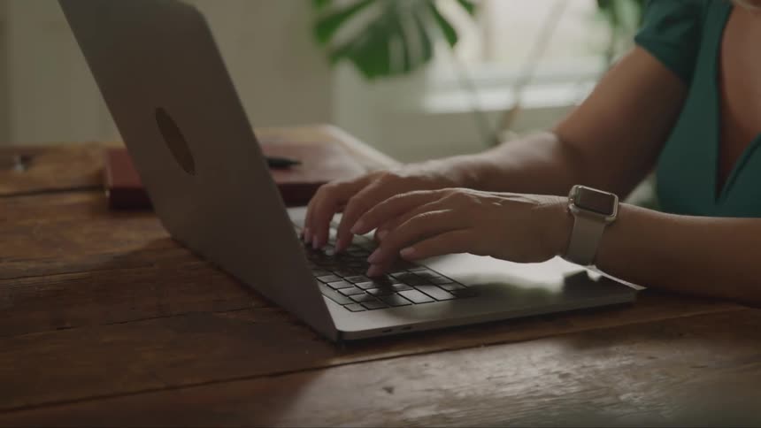A woman is typing on her laptop at her desk