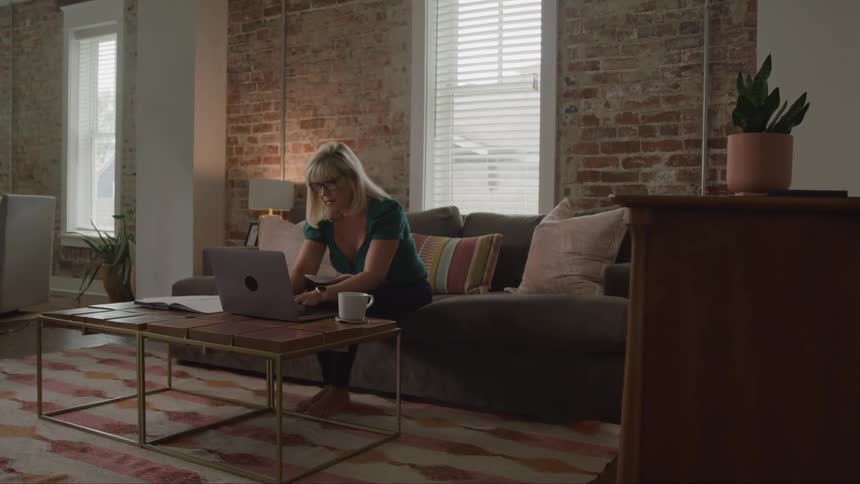 Woman using a laptop while sitting on a sofa in a room with exposed brick walls