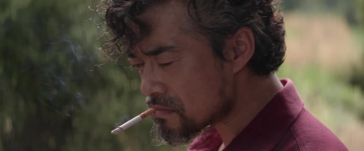 A disheveled asian man smokes a cigarette