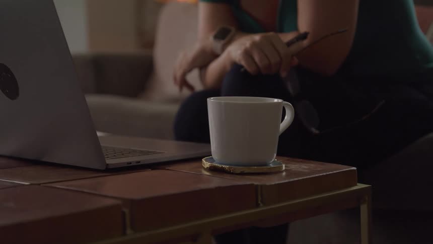 A woman sitting in her living room working on a laptop with a coffee mug on the side table