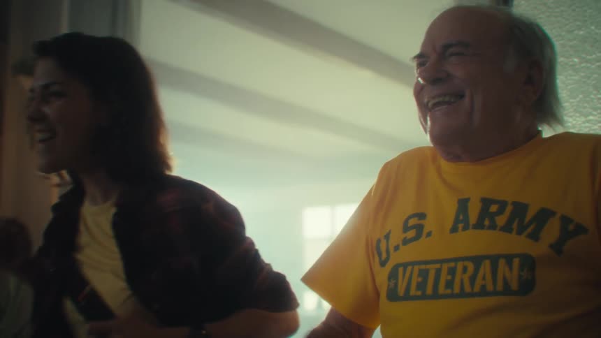 A young woman sits on a chair beside an elderly man in the living room watching a game they both suddenly become excited by the result at midday