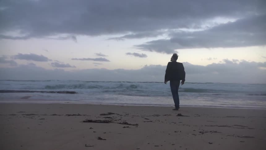 Man walks on the sand towards the water on a cloudy day