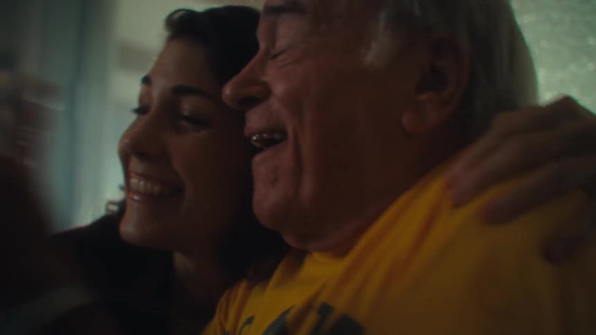 A young woman and an elderly man celebrate winning while watching tv in a living room during daytime