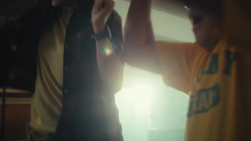 An elderly man wearing a yellow tshirt sits beside a young woman both becoming very excited while watching a game indoors at midday