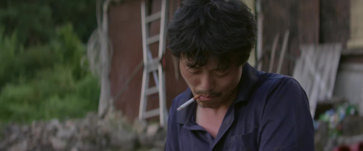 A man in a blue shirt smokes and ties a bundle of sticks