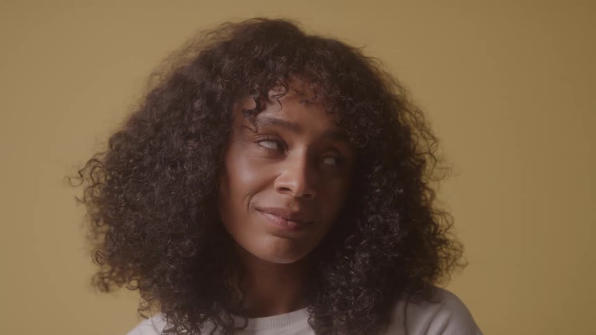 A young woman with curly hair and a smile sits inside a room with yellow walls