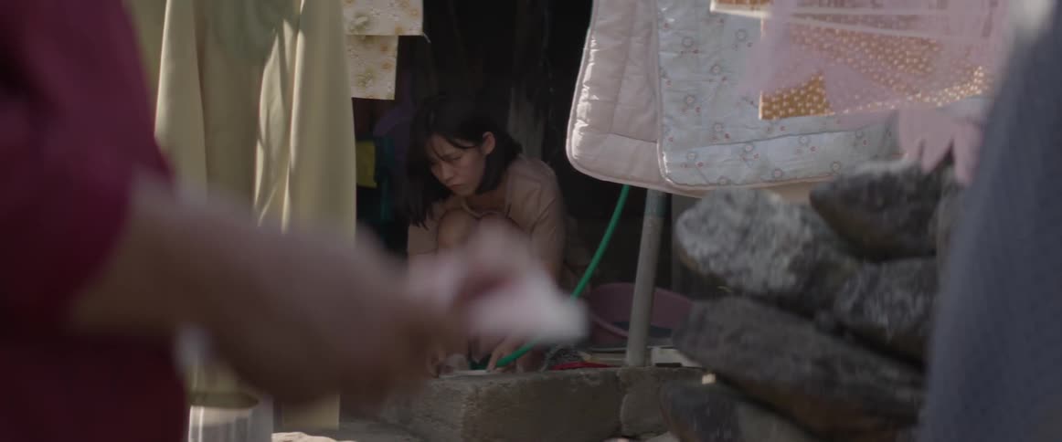 An asian woman washes a plate with a hose