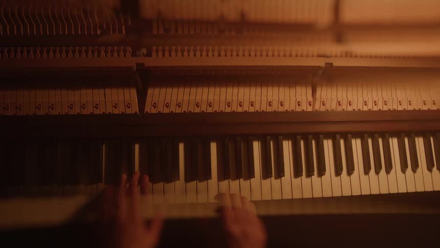 Hands playing piano keys with exposed strings and hammers