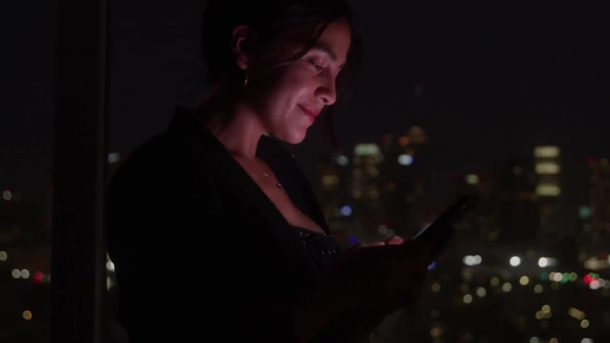 Woman using her phone at night with the city lights in the background