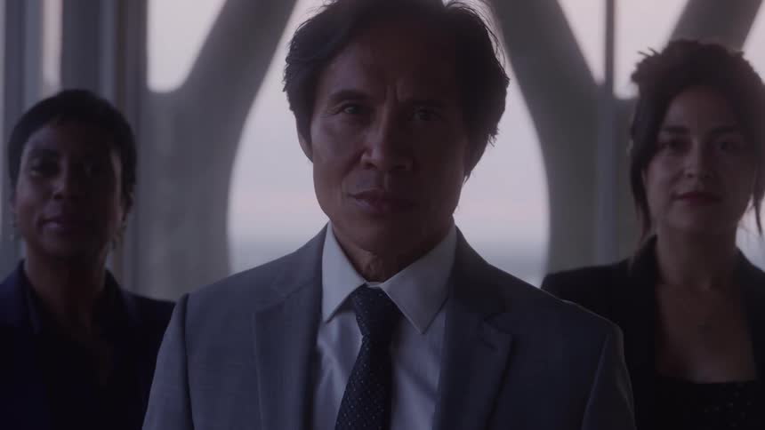 Man in a suit and tie with two women in the background in a corporate setting