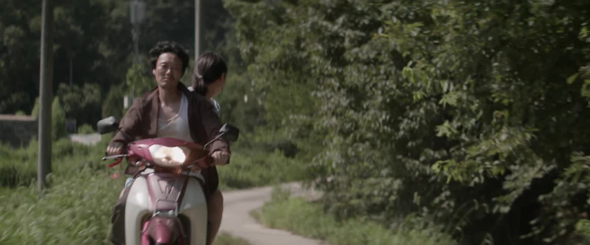 An asian woman looks nervously riding a motorcycle behind a man