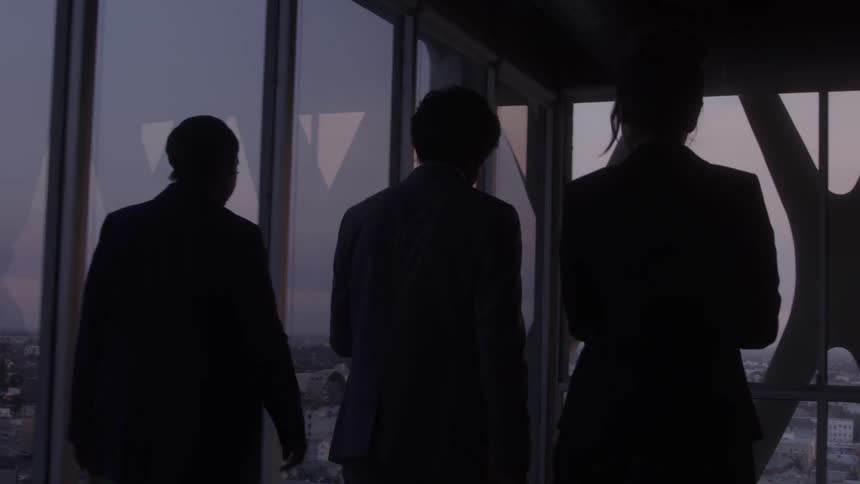 Three office workers two men and one woman walking down a conference room discussing at sunset