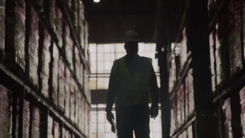 Silhouette of a worker wearing a hard hat walking between warehouse shelves