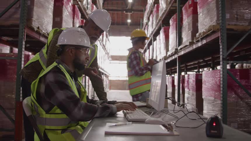 Woman walking past a warehouse in the background and two men interacting in front of a computer