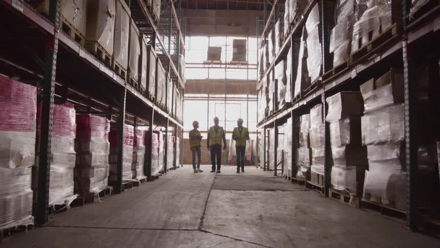 Three workers walk together while conversing in a warehouse during daytime