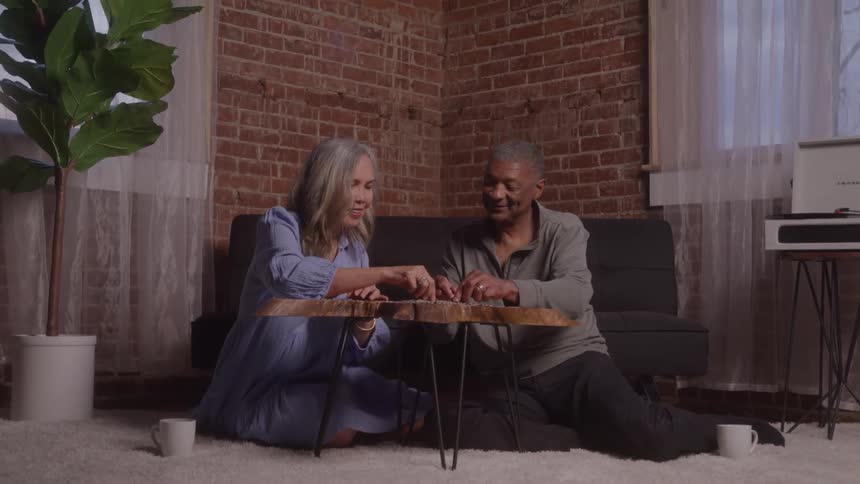 A couple sits on the living room floor smiling as they play a fun game together
