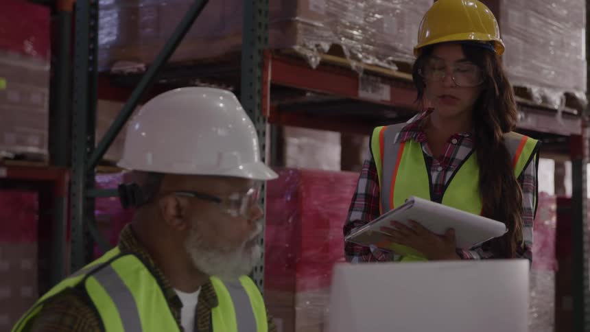Workers wearing helmets and reflective vests talking in a warehouse