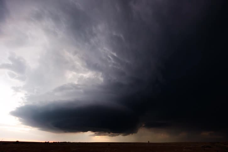 A dramatic supercell storm cloud swirls over the horizon at sunset