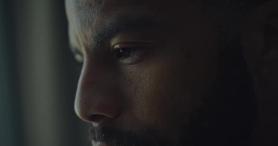 A closeup shot of a mans face focused on his eyes and nose shows him looking down and to the side the light illuminates the left side of his face while the right side remains in shadow
