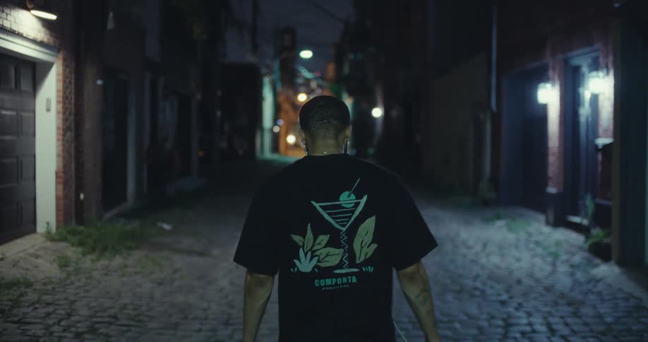 A man walks alone down a dimly lit cobblestone alley at night
