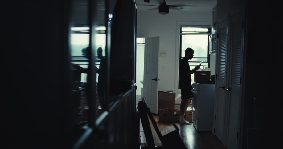 Person stands in the kitchen reading something while unpacking boxes
