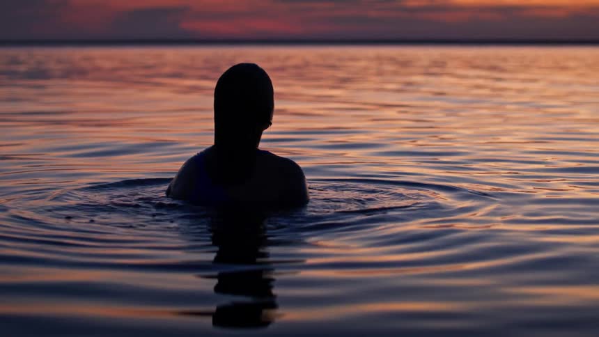 A woman floats in calm water at sunset surrounded by golden ripples