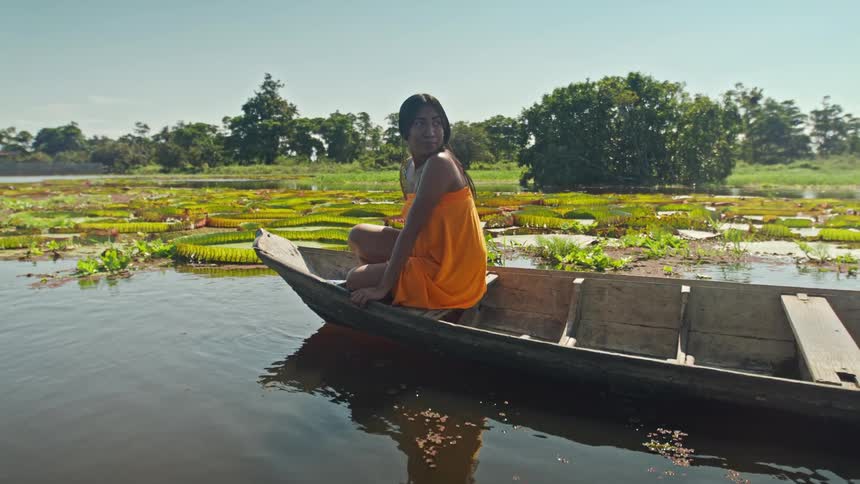 Woman sits in a wooden boat on a river near aquatic plants