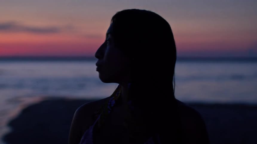 A womans silhouette against a vivid sunset over calm water