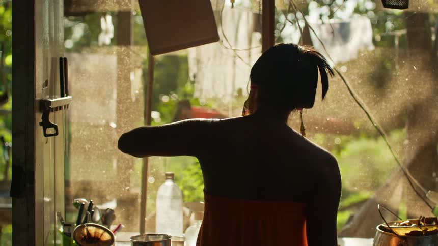 Woman in orange dress cooking in a sunlit kitchen