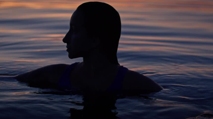 A silhouette personfloats in calm water at sunset