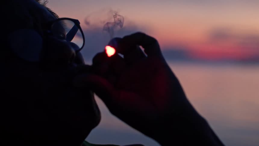 Person in silhouette smokes with the sunset in the background