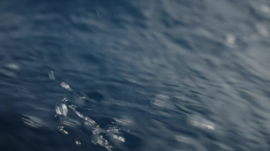 A view from a low angle shows the surface of the dark blue ocean with waves and ripples moving on top of the water