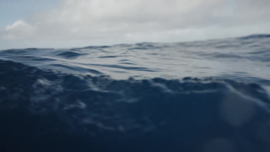 The video shows a lowangle shot of the open ocean with the waters surface undulating under a cloudy sky the cameras perspective is close to the water emphasizing the deep blue color and the gentle movement of the waves